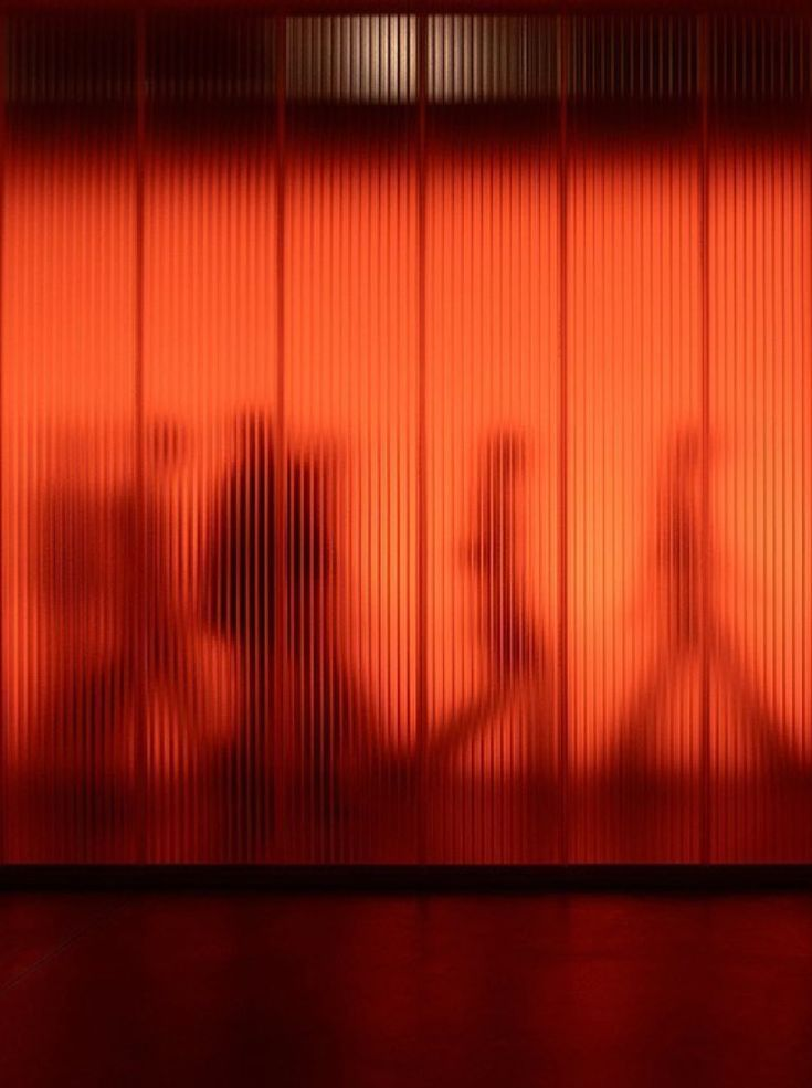 Figures in silhouette behind a signal-orange fluted screen