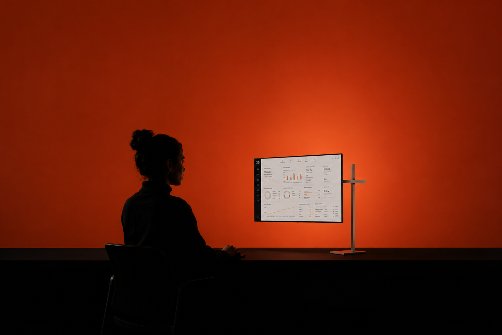 An analyst at a desk reading the XS dashboard against a signal-orange wall
