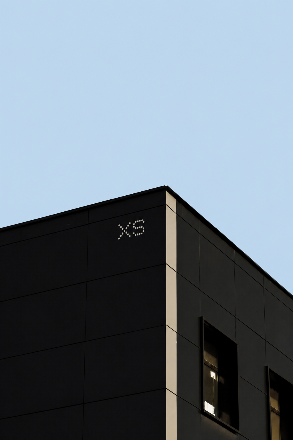 XS dot-matrix mark on a black building corner against sky